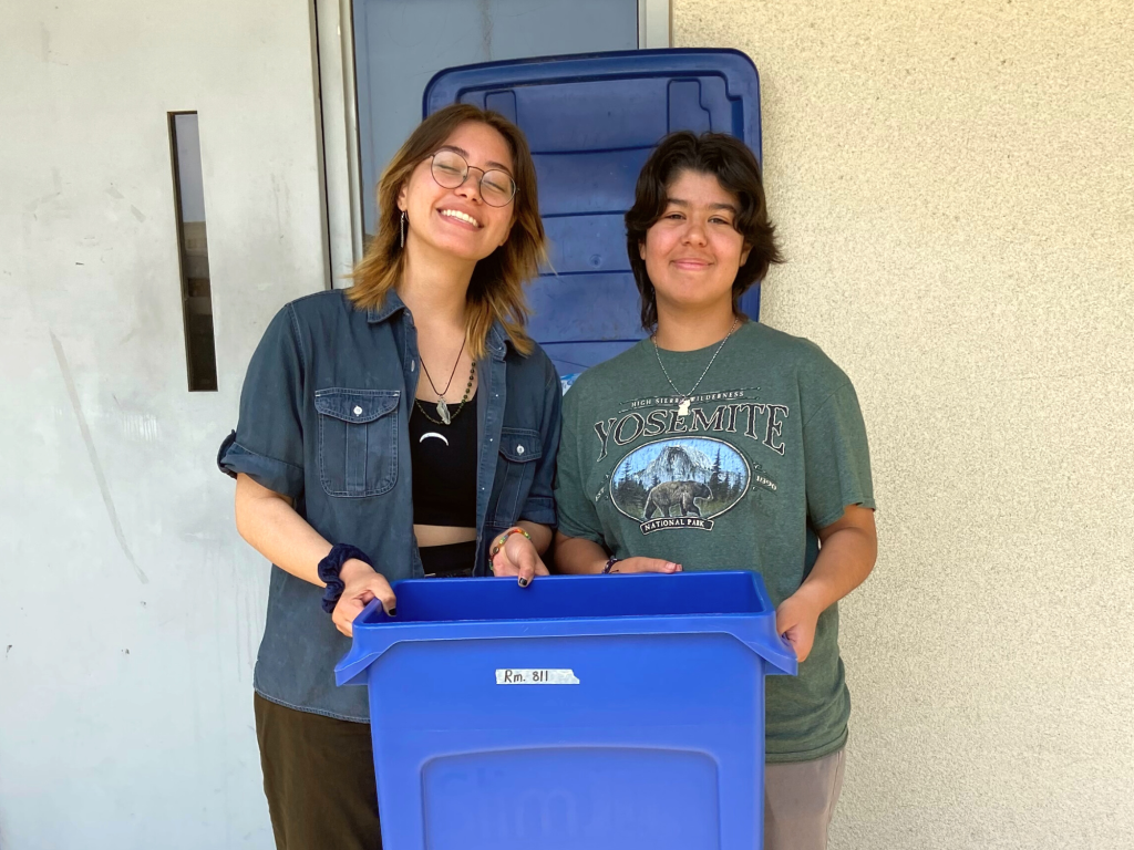 2 students pose with a recycling bin